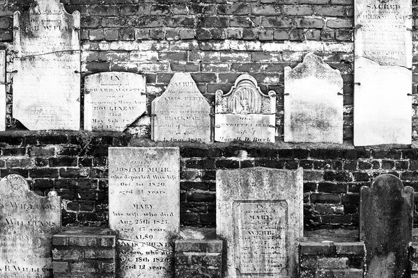 Black and white photograph of a row of very old gravestones mounted on a brick wall in Savannah's historic Colonial Cemetery, established in 1750.