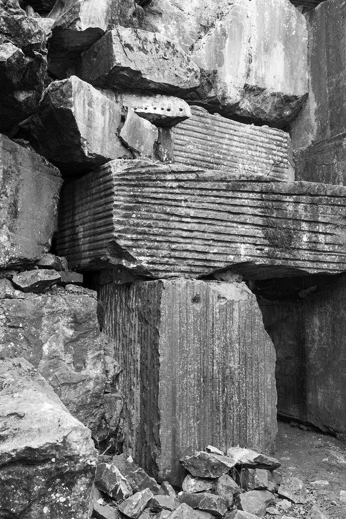 Black and white landscape photograph of textured marble rubble and boulders in an abandoned marble quarry.