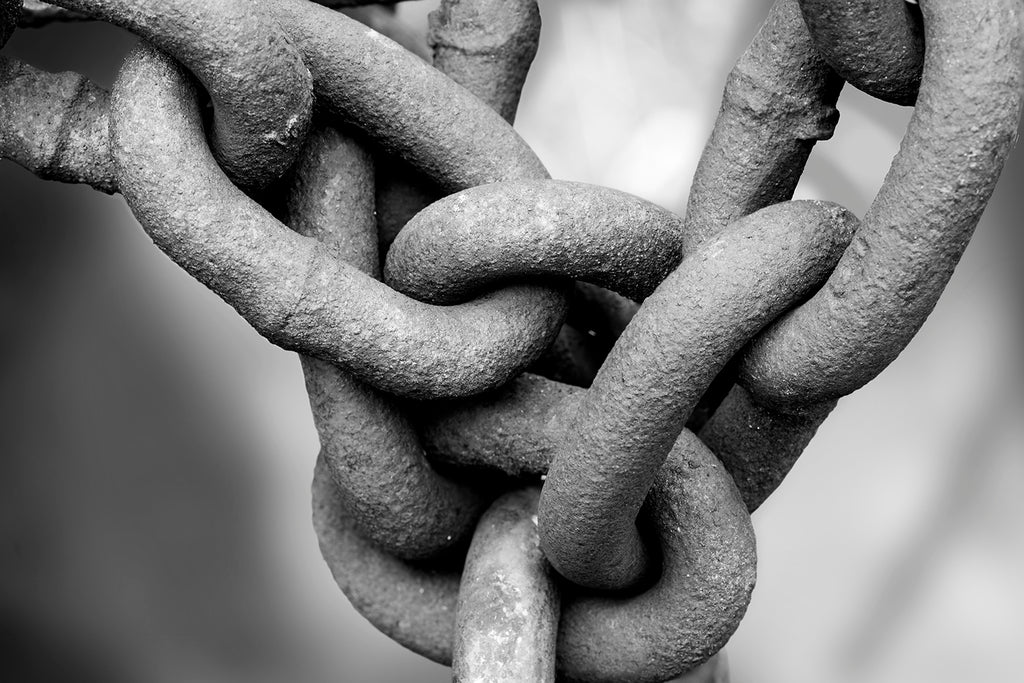 Black and white macro photograph of a rusty chain with textured surfaces of the links shown in extreme detail.