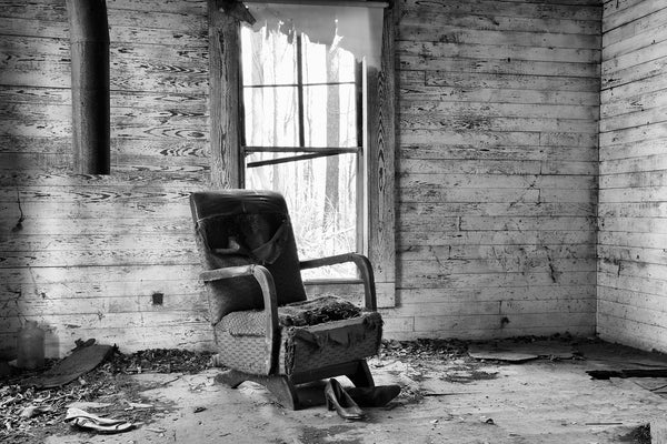 Black and white photograph of an old ruined chair and women's shoes inside an abandoned old house in the countryside.