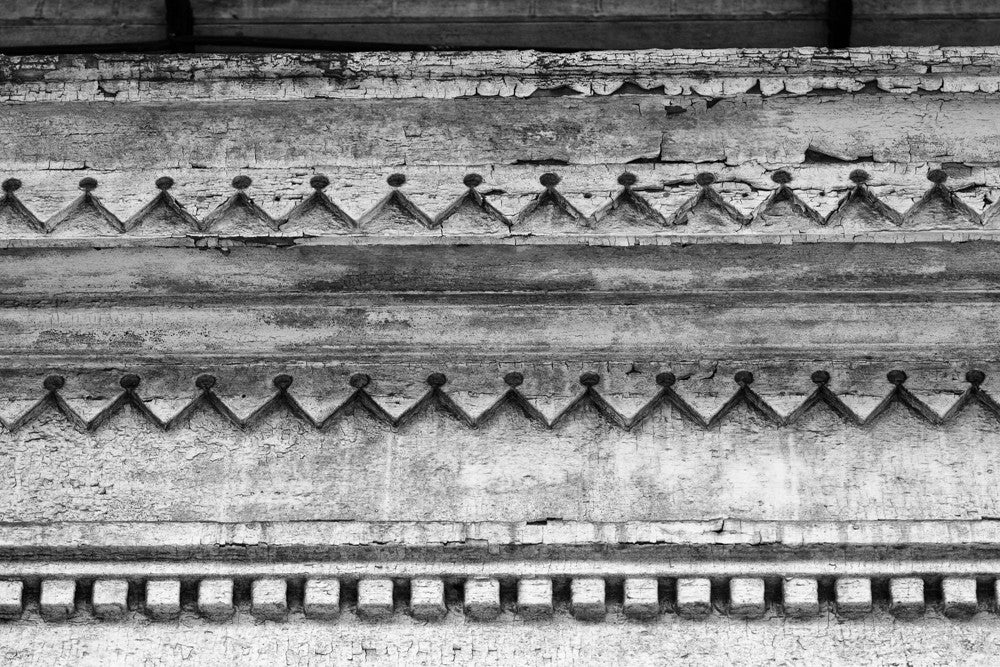 Black and white architectural detail photograph of decorative but decaying woodwork on the eave of an abandoned house in the New Orleans French Quarter.
