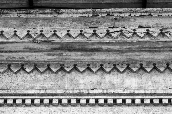 Black and white architectural detail photograph of decorative but decaying woodwork on the eave of an abandoned house in the New Orleans French Quarter.