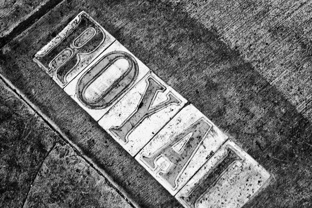 Black and white fine art photograph of dirty Royal street sign letters in a sidewalk in the French Quarter of New Orleans, Louisiana.