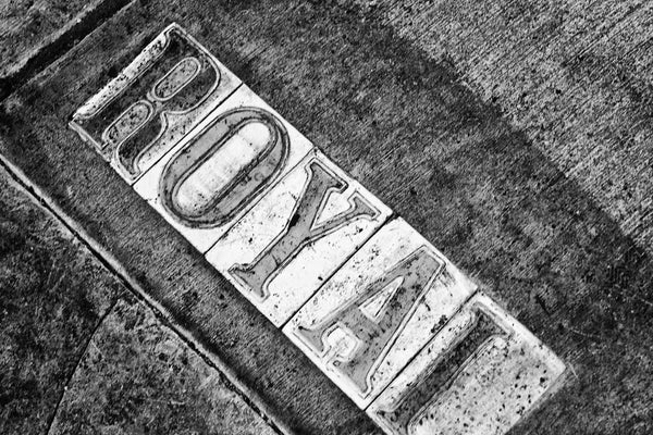 Black and white fine art photograph of dirty Royal street sign letters in a sidewalk in the French Quarter of New Orleans, Louisiana.