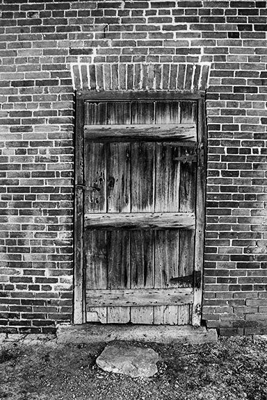 Black and white photograph of a wooden door in an old brick outbuilding on the property of the historic Carter House in Franklin, Tennessee. The house and its property was the site of bloody fighting during the battle of Franklin, and original musket ball holes can still be seen in the house and sheds.