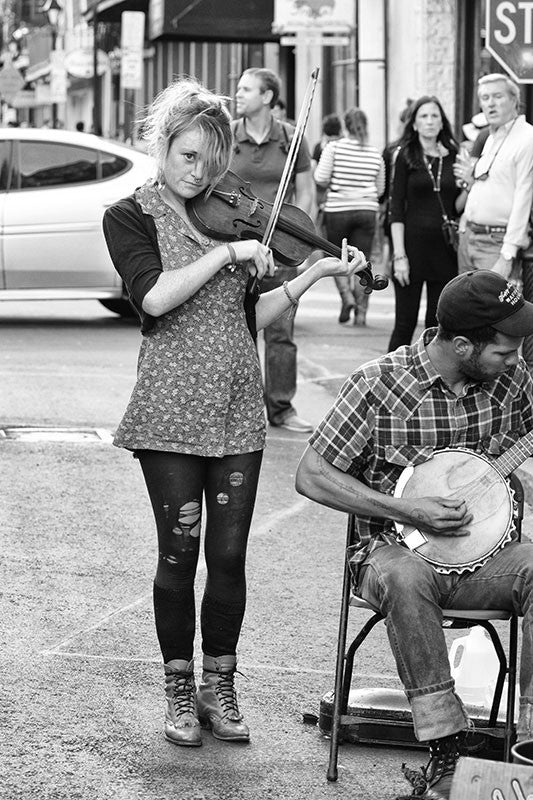 Black and white fine art photograph of a street musician playing a violin with her band in the New Orleans French Quarter.