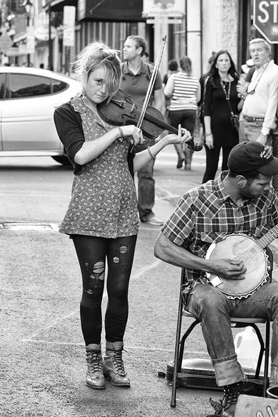 Black and white fine art photograph of a street musician playing a violin with her band in the New Orleans French Quarter.