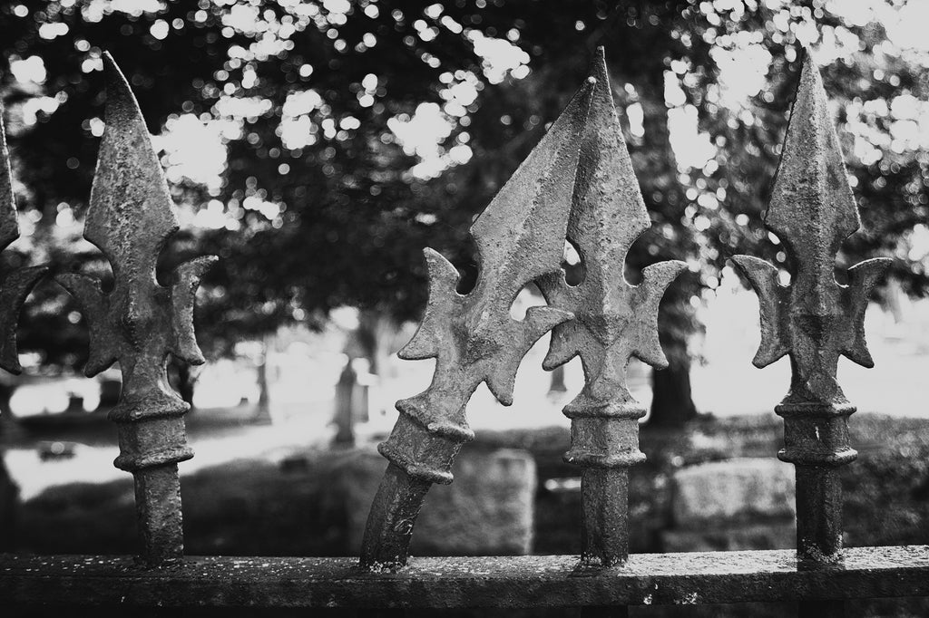 Black and white photograph of an antique iron fence with a finial spike bent and leaning on the neighboring spike.