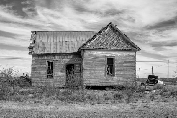 Black and white photograph of an abandoned old house with just a small amount of white paint still showing on its weathered wooden clapboards.