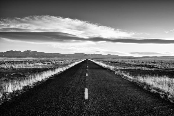 Black and white landscape photograph of a highway to the distant mountains seen in the first morning light.