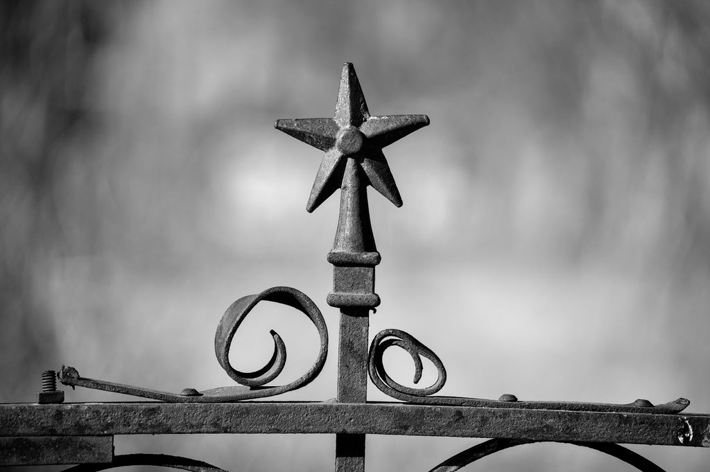 Black and white detail photograph of a rusty ironwork fence surrounding an abandoned old house in a small town far West Texas.