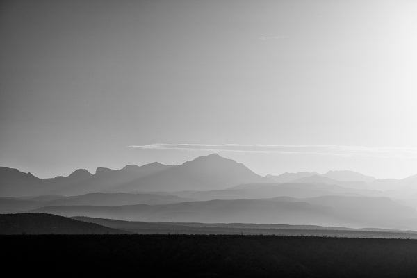 Black and white landscape photograph of layers of hazy distant mountains seen in the first morning light.