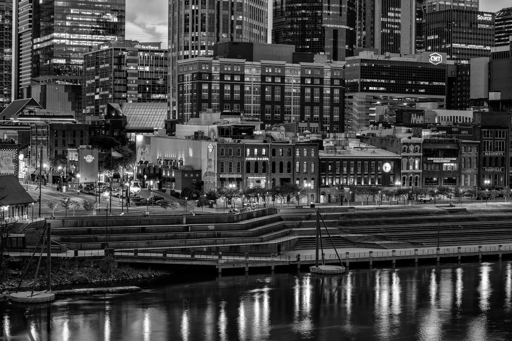 Black and white photograph of Nashville's historic waterfront and Broadway entertainment district at night with lights reflecting in the Cumberland River.