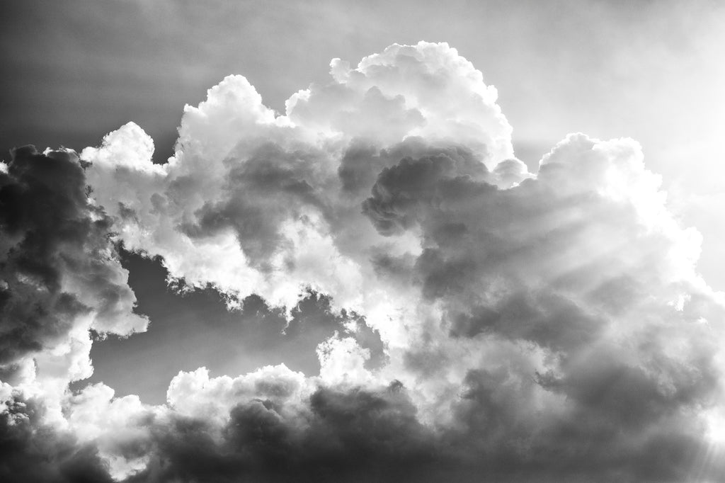 Black and white photograph of big summer clouds with sunbeams and a gap in their midst.