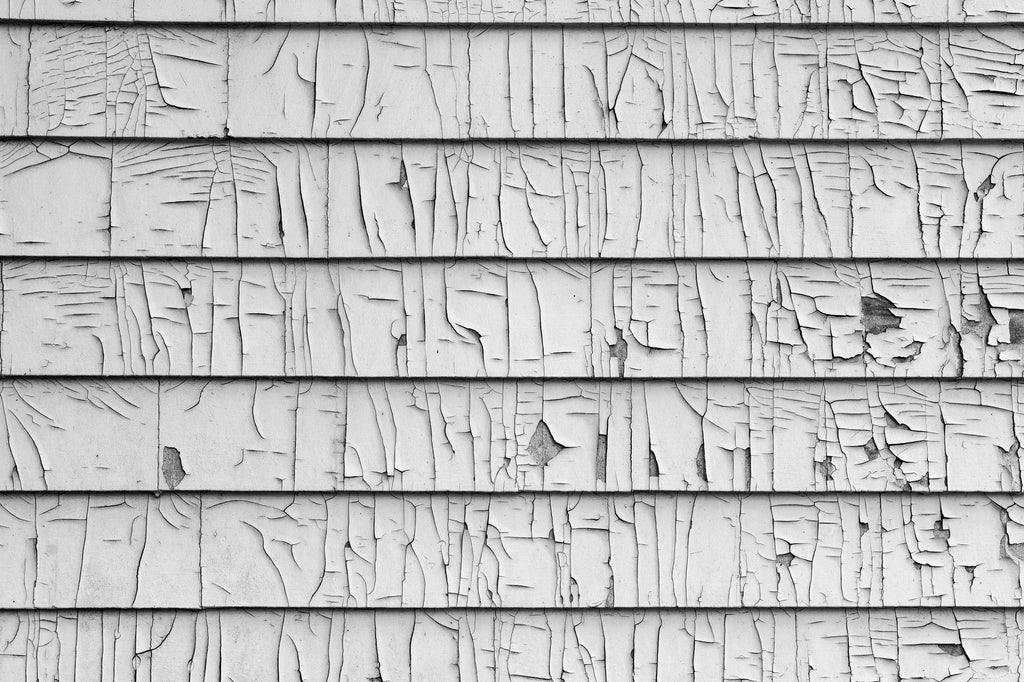 Black and white photograph of rhythmic cracks in the paint on the clapboard exterior of an abandoned old house.