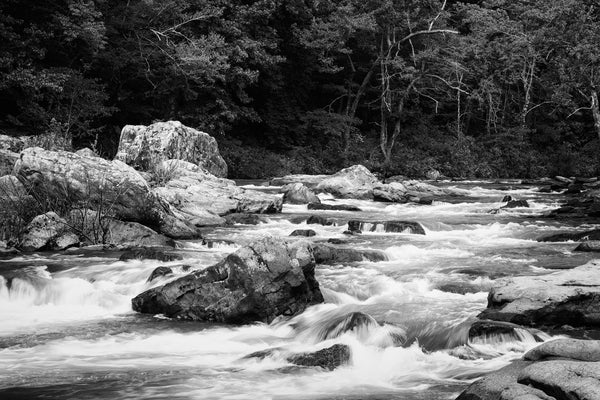 Black and white landscape photograph of a beautiful river rushing over and around big rocks.