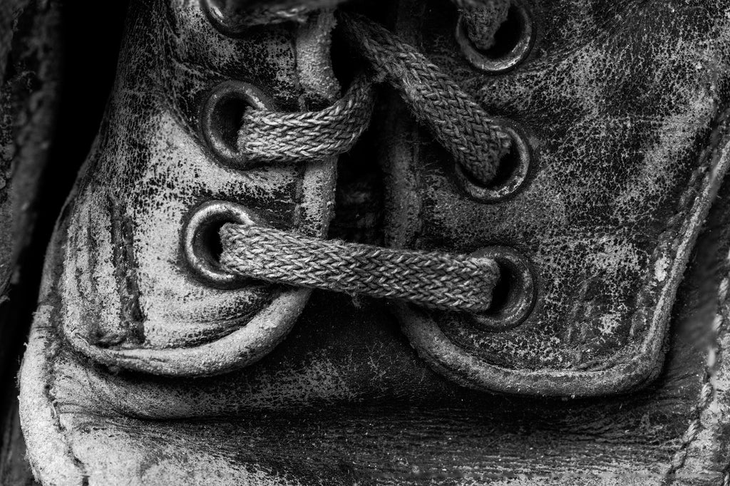 Dramatic black and white detail photograph of the laces and eyelets on an old tattered leather boot.