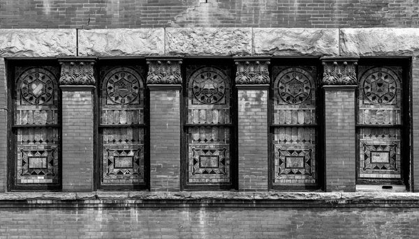 Black and white photograph of five stained glass windows separated by brick pilasters with Corinthian capitals seen on the front of the Third Presbyterian Church, built 1887 in South Wheeling, West Virginia.