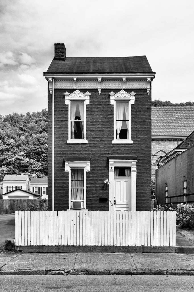 Black and white photograph of a little vintage brick house with a white picket fence.