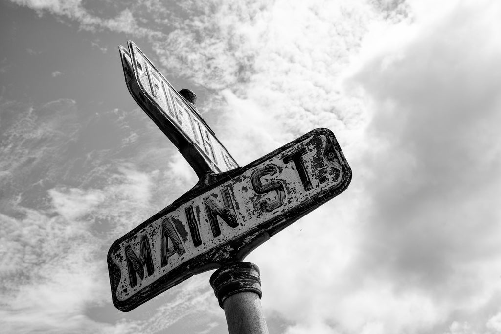 Black and white photograph of an old street sign at the corner of Main Street and Fifth Street in a small midwestern town.