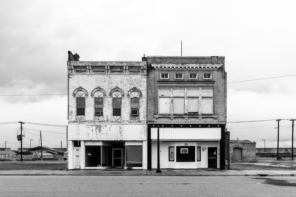 Black and white photograph of the last two buildings still standing on a vacant city block that was once lined with businesses.