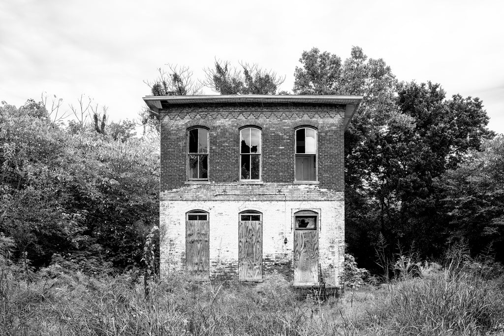 Black and white photograph of a historic abandoned house in an overgrown neighborhood along 8th Street in Cairo, Illinois.