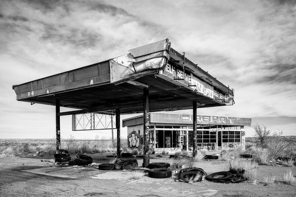 Black and white photograph of an abandoned vandalized service station in the wide-open landscape of the Texas Panhandle.