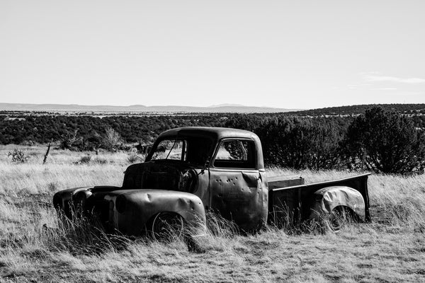 Black and white photograph of an abandoned old pickup truck riddled with bullet holes, seen in the high desert of New Mexico.