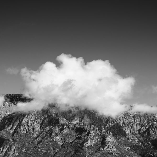 Black and white photograph of clouds gathered around a mountain top in the American Southwest