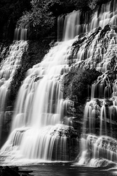 Black and white landscape photograph featuring a tall cascading white waterfall blurred by the motion of the falling water.