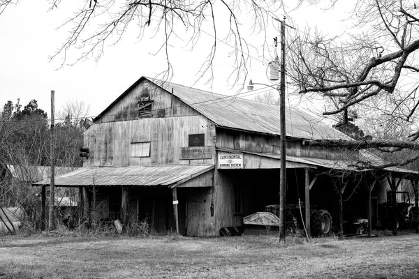Black and white photograph of an old cotton gin building in a small southern town with signs that say "Continental Ginning System" and "Continental Golden Comet System."