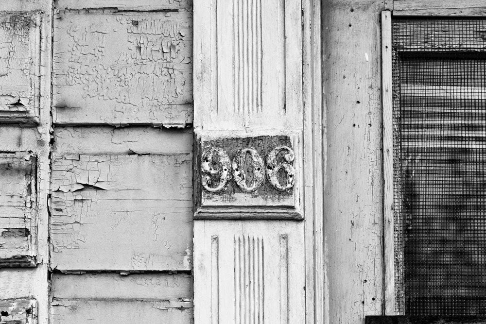 Black and white architectural detail photograph of a weathered, peeling door with house number 906, seen in the French Quarter of New Orleans.