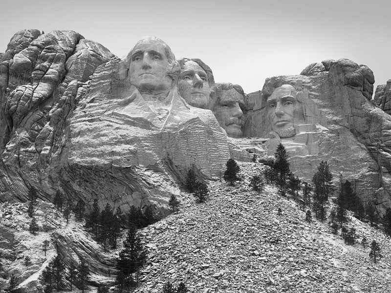 Black and white landscape photograph of Mt. Rushmore with a light dusting of snow.