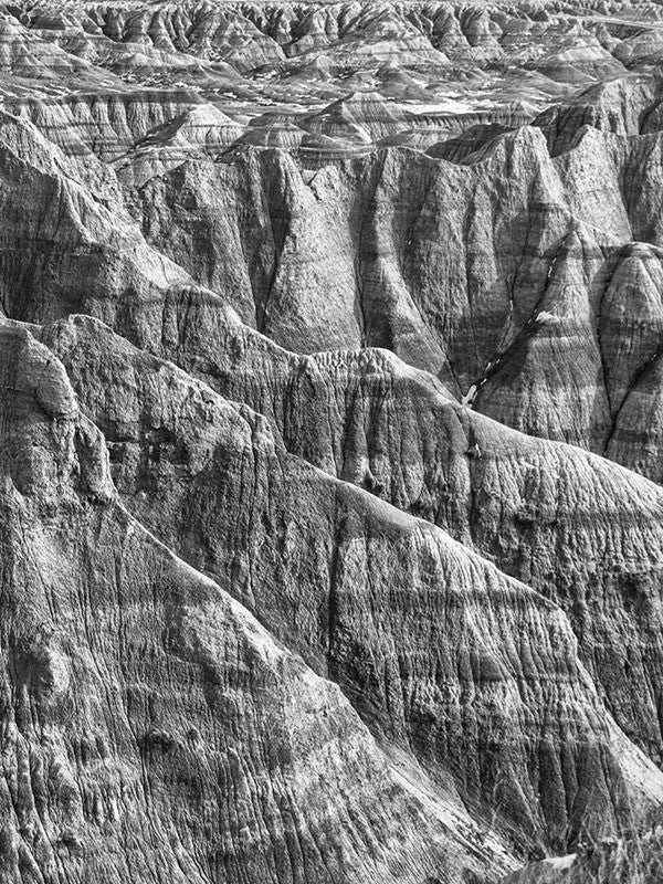 Black and white landscape photograph of the rugged, wrinkled, and treeless terrain at the Badlands of South Dakota.