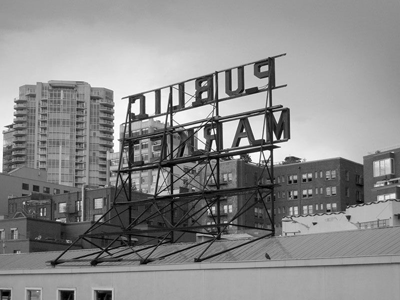 Black and white photograph the skyline of Seattle with the famous Public Market sign seen in reverse. This photograph was sold in Urban Outfitters stores and online as part of their Wall Art Canvas selection.