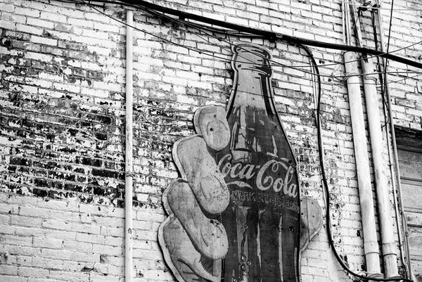 Black and white photograph of a vintage Coca Cola sign featuring a large hand holding a bottle of Coke in a grimy alley in downtown Nashville, Tennessee. 