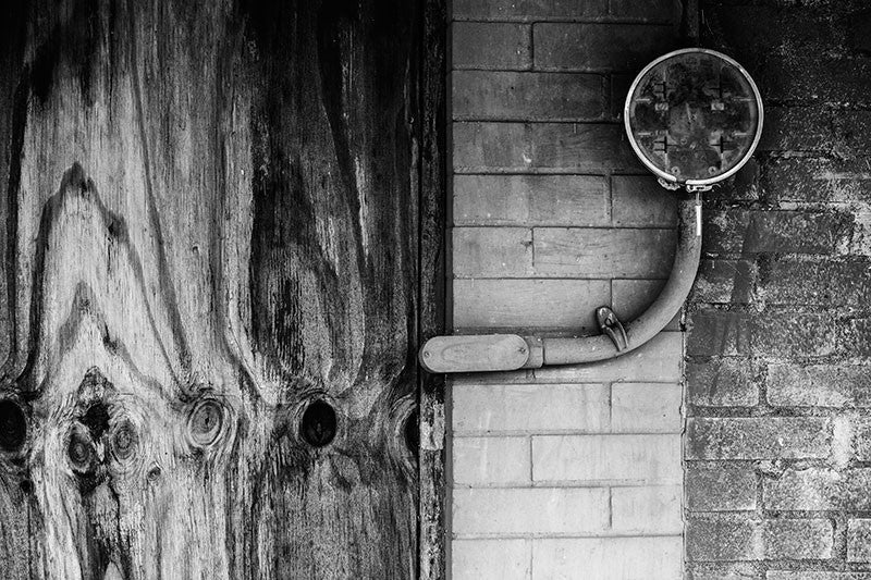 Black and white detail photograph of plywood, bricks, and an unused utility connection on an abandoned storefront in the deserted downtown area of Adams, Tennessee.