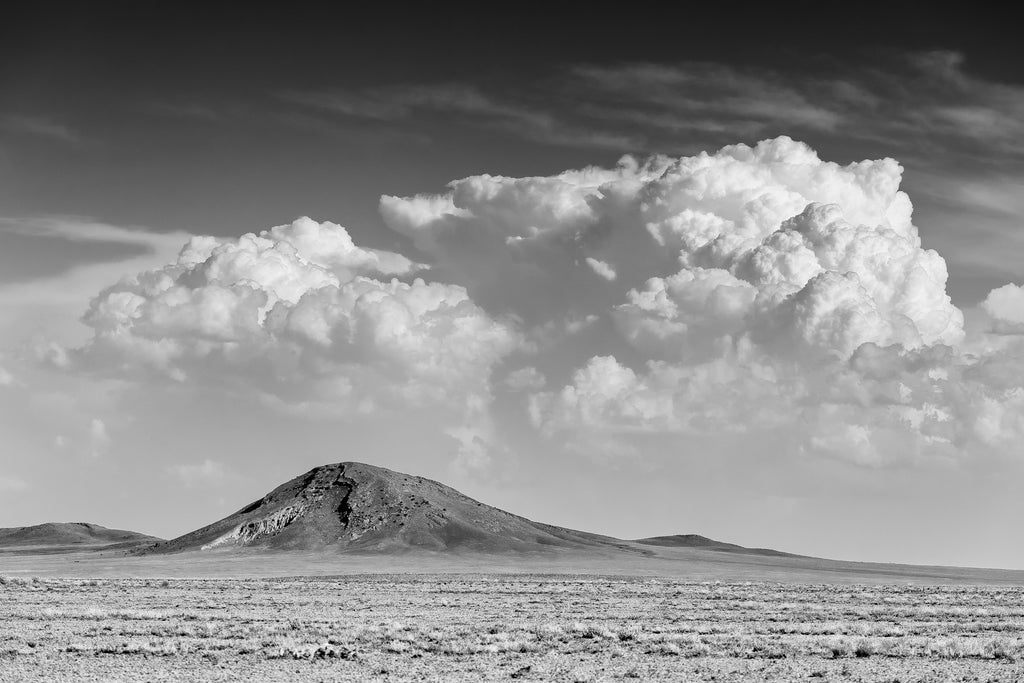 Black and white landscape photograph of the beautiful New Mexico desert featuring a mountain beneath a dramatic bank of late afternoon clouds.