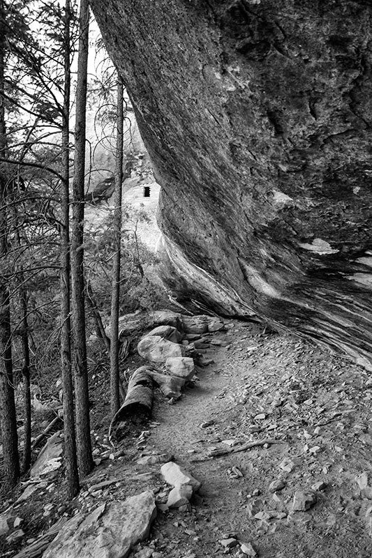 Black and white landscape photograph taken on the Petroglyph Trail at Mesa Verde, Colorado. Just upper left of center can be seen the window of an ancient cliff dwelling.