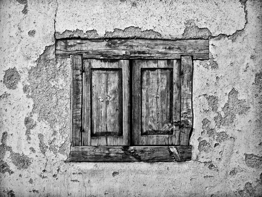 Black and white architectural detail photograph of the textural adobe walls and shuttered window of an old house in Taos, New Mexico, where Kit Carson once lived.