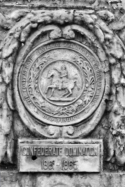 Black and white photograph of an ornate street pole crest, part of a series illustrating the nations that have ruled over Louisiana in the past, seen along Basin Street in New Orleans. The metallic sign says, "Confederate Domination 1861 - 1865."