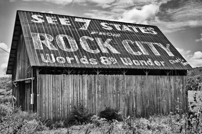 Black and white photograph of a rural barn featuring the famous and historic See Rock City ad painted on its tin roof.