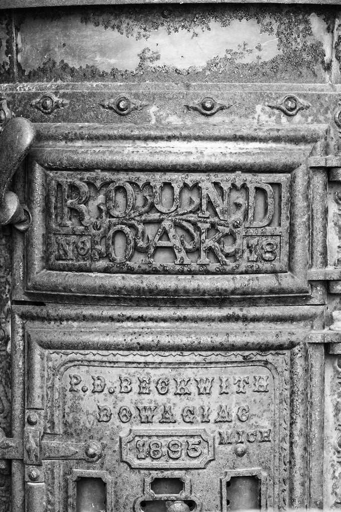 Black and white photograph of a rusty, antique Round Oak stove found in a collapsed building