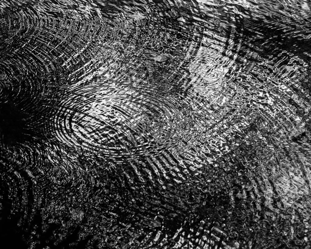 Black and white photograph of complex, overlapping river ripples