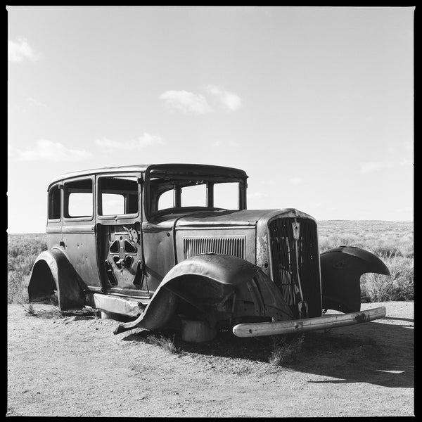 Black and white photograph of a rusty antique 1932 Studebaker installed on a historic alignment of Route 66 within a National Park in the Arizona desert.