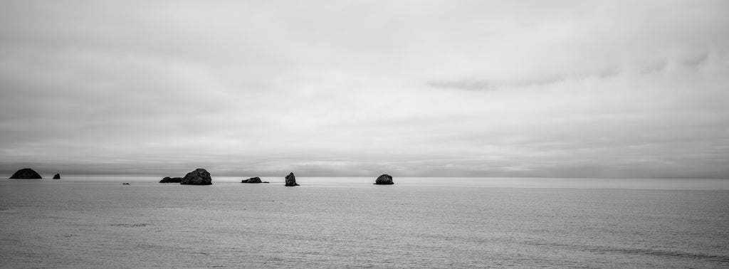 Black and white panoramic landscape photograph of sea stacks in the Pacific Ocean off the coast of Oregon.