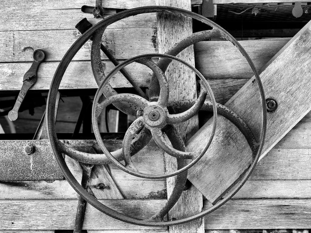 Black and white photograph of a pulley wheels on the side of a big wooden antique farm machine.