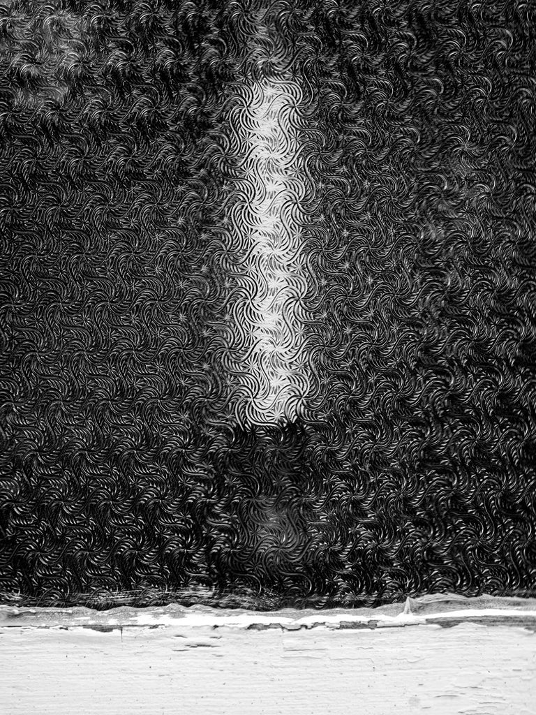 Black and white photograph of a candle made almost abstract by the heavily textured window glass of the historic Bethel Church in the beautiful Adirondack region of upstate New York.