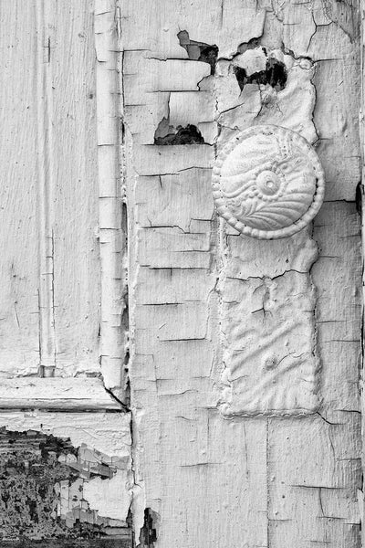 Black and white photograph of an antique doorknob on an abandoned building covered in layers of cracked paint.