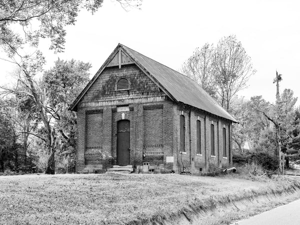 Black and white photograph of an abandoned one-room schoolhouse named "School No. 4,"  found along a backroad in the American South. On the cornerstone, dated 1892, are listed the names, O. Raber (title unclear - possibly Teacher or Treasurer), J. Ransley, Architect, and J.A. Koch, Builder.